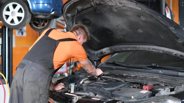 An adult man in a gray-orange uniform works with a car. A car mechanic examines a car engine. 4k video