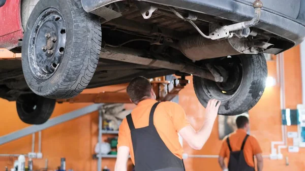 Car service, car on the lift in a specialized service. The mechanic checks the condition of the car suspension. Rear view