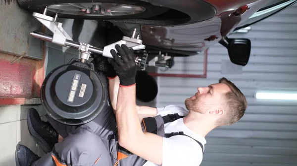 Vertical video. A car mechanic in a workshop attaches a jack to a car. Professional car repair. Wheel replacement