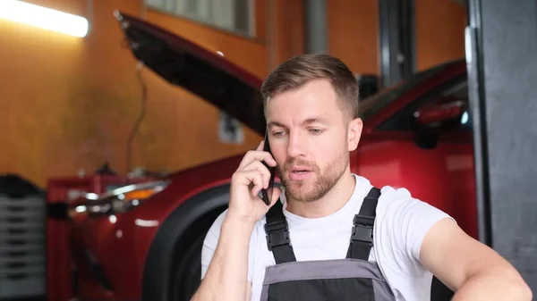 一位恼怒的汽车修理工坐在一家汽车修理店里 在电话里粗鲁地与人交谈 一个令人不快的电话交谈 挂断电话 — 图库照片
