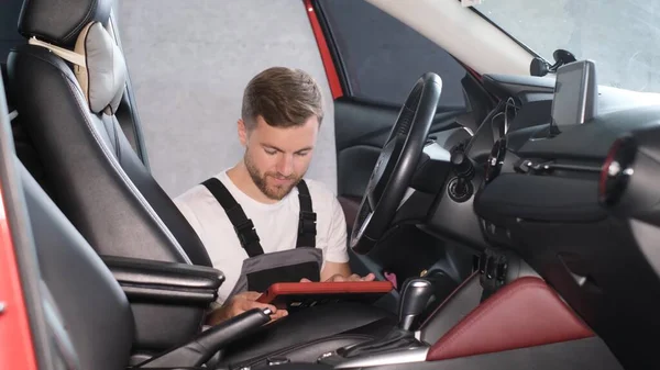 一位年轻的美国汽车修理工用平板电脑检查汽车的技术状况 在新车上安装Gps导航器 — 图库照片