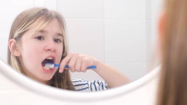 Genç bir kız banyo aynasının önünde dişlerini dikkatlice fırçalar. Çocukların diş sağlığı.
