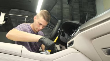 Araba yıkama servisi. Genç bir işçi yeni bir arabanın şanzımanını fırçayla temizliyor..