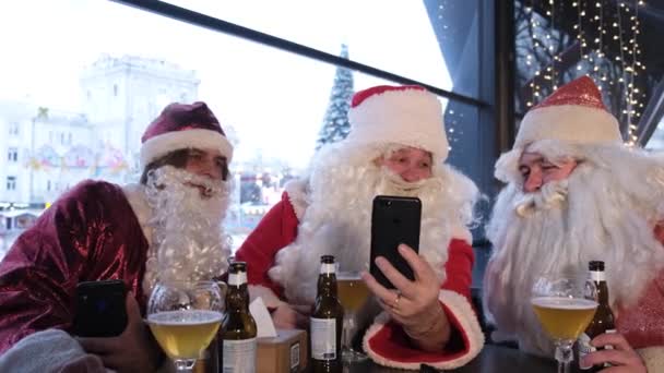 3サンタクロースは 彼の目を大きく開いてスマートフォンの画面を見ています サンタクロースの衣装を着た男性がカフェで休んでいます クリスマスタイム — ストック動画
