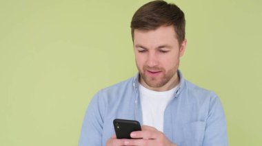 Young European man with smartphone in hands pointing hands at gadget display isolated on yellow-green studio background.