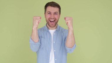 Handsome smiling american man in denim shirt white t-shirt isolated on yellow-green background in studio. the man rejoices and raises his hands