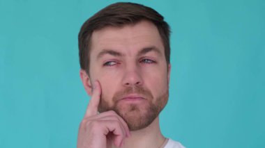 Close up portrait of pensive man on turquoise background in studio. Guy thinking touching chin, reflection pensiveness