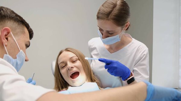 Modern dentistry. A young doctor and an assistant treat the teeth of a young woman. Painless dental treatment. Timely treatment of teeth.