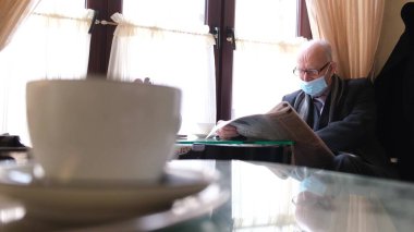 Gri saçlı, gözlüklü ve siyah ceketli bir adam kafede kitap okurken yeni bir gazete okuyor. Gerçek zamanlı. 4k video