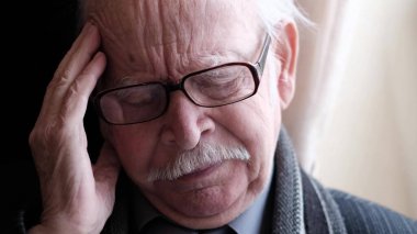 Tired, depressed older gray-haired man experiencing headache and loneliness. The old man touches his forehead, suffers from severe headaches. High quality 4k video
