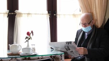 The waiter serves in the cafe, he brings his grandfather coffee. Gray-haired grandfather is resting in a cafe and reading a newspaper
