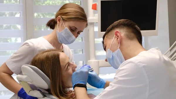 在牙科诊所一位医生和一位助手治疗一位年轻妇女的牙齿 及时治疗牙齿 口腔疾病 — 图库照片
