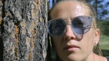 Portrait of a girl with glasses near the tree. Camera zooms out, close-up