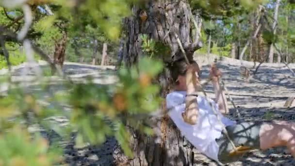 Girl swinging on a rope swing in the shade of a tree on a sunny summer day — Video