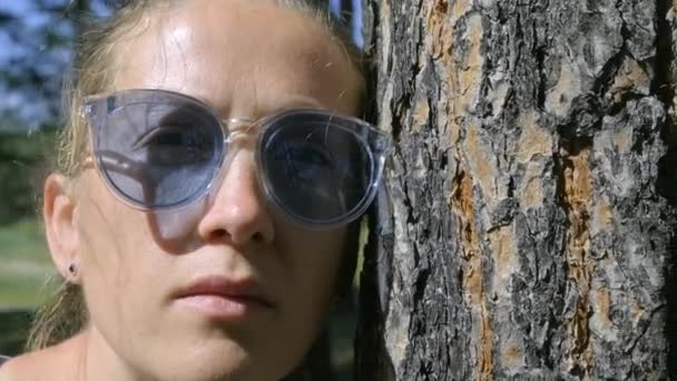 一个女孩靠在树干上看着摄像机的画像 风吹乱了一个年轻女人的头发慢动作 变焦了 — 图库视频影像