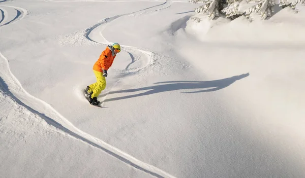 Snowboarder in orange jacket and yellow pants drives down the piste. Winter sport and recreation, leisure outdoor activities. Off-piste snowboarding. — Fotografia de Stock