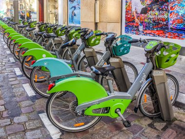 PARIS, FRANCE - FEBRUARY 17, 2020. Electric rental bikes, green and gray, locked on their chargers. Velib rental station. Row Electric-assisted bicycle, ecological alternative against pollution. Urban transport.