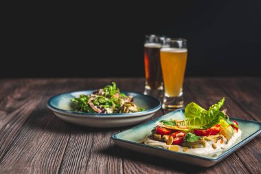İki bardak bira ve sonbahar ya da kırsal ahşap masada siyah arka planda düşen yiyecekler. Bira, buğday, koyu hafif bira, bira konsepti. Ekim Festivali.