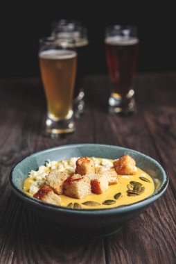 İki bardak bira ve sonbahar ya da kırsal ahşap masada siyah arka planda düşen yiyecekler. Bira, buğday, koyu hafif bira, bira konsepti. Ekim Festivali. Balkabağı kremalı çorba..