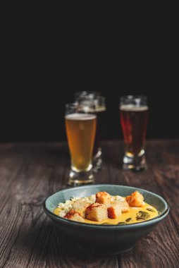 İki bardak bira ve sonbahar ya da kırsal ahşap masada siyah arka planda düşen yiyecekler. Bira, buğday, koyu hafif bira, bira konsepti. Ekim Festivali. Balkabağı kremalı çorba..