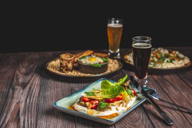 İki bardak bira ve sonbahar ya da kırsal ahşap masada siyah arka planda düşen yiyecekler. Bira, buğday, koyu hafif bira, bira konsepti. Ekim Festivali.