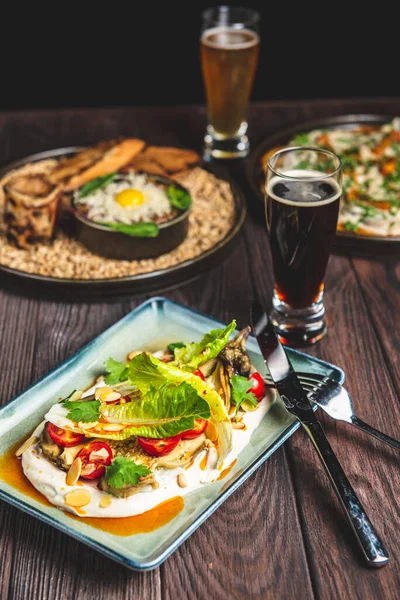 İki bardak bira ve sonbahar ya da kırsal ahşap masada siyah arka planda düşen yiyecekler. Bira, buğday, koyu hafif bira, bira konsepti. Ekim Festivali.