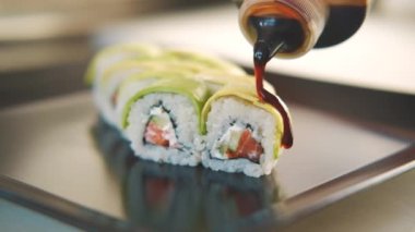 Suşi Green Dragon 'un hazırlanması, şefin suşi yapması, siyah tabakta servis edilmesi, rulonun üzerine sos dökmesi. Japon mutfağı kavramı.