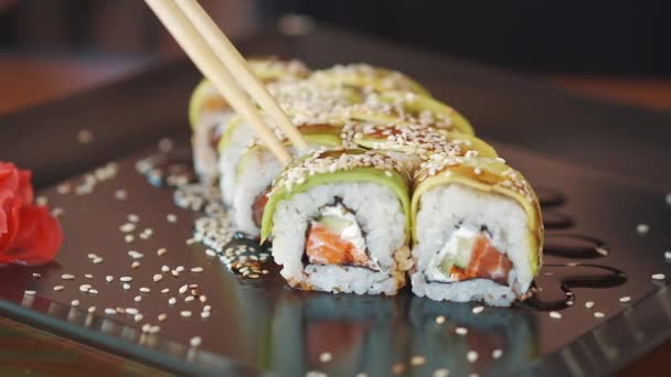 寿司職人が巻き寿司を作る グリーンドラゴン をブラックプレートに盛り付けます 寿司を箸で一口食べる 日本料理のコンセプト — ストック動画