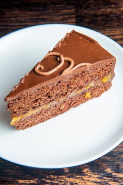 Kayısı reçelli Avusturya usulü çikolatalı tatlı vaizi. Geleneksel Sacher pastasından bir dilim, siyah ahşap bir masada beyaz tabakta servis edilir. Lezzetli çikolatalı pasta, geleneksel tarif..