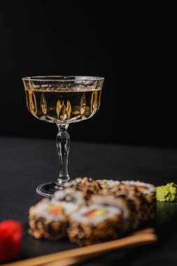 Wasabi ve zencefil ile servis edilen siyah desenli bir arka planda suşi rulosu. Estetik gıda, Japon mutfağı konsepti. Suşi reklamı. Bir bardak alkolle birlikte..