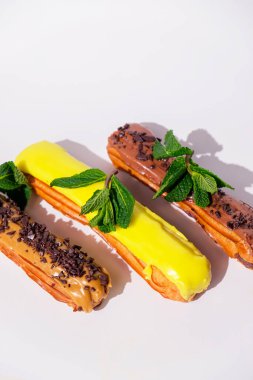 Çikolata kapaklı ve farklı dolgulu Fransız ekleriymiş. Geleneksel tarif, Fransız mutfağı. Saf beyaz arka planda karamel, çikolata ve limon ekleriydi. Kopyalama alanı olan dikey pankart.