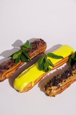 Çikolata kapaklı ve farklı dolgulu Fransız ekleriymiş. Geleneksel tarif, Fransız mutfağı. Saf beyaz arka planda karamel, çikolata ve limon ekleriydi. Kopyalama alanı olan dikey pankart.