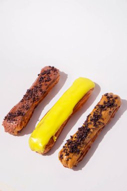 Çikolata kapaklı ve farklı dolgulu Fransız ekleriymiş. Geleneksel tarif, Fransız mutfağı. Saf beyaz arka planda karamel, çikolata ve limon ekleriydi. Kopyalama alanı olan dikey pankart.