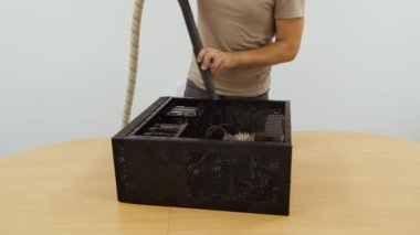 Bilgisayar ekipmanlarını tamir ve temizleme servisi. Kahverengi tişörtlü bir adam elektrikli süpürge kullanarak bir masaüstü bilgisayarını temizliyor.