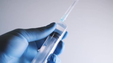 Elinde şırınga olan mavi eldiveni ver. Elinde keskin bir iğne olan şırınga. Aşı konsepti. Doktor, koruyucu kapağı iğneden çıkarır.