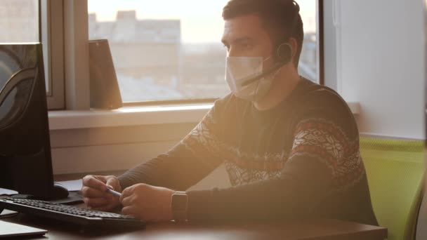 Datorträning online under coronaviruspandemin. Människan i medicinsk mask utför arbete vid en dator. — Stockvideo