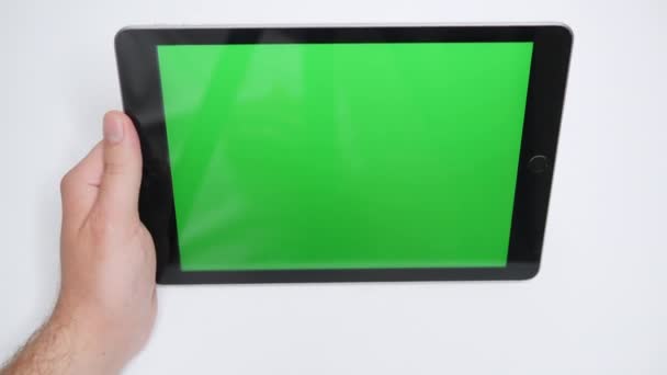 Uma mão de homem coloca o tablet em uma mesa branca e liga assistindo a um vídeo ou filme. Close-up de um tablet moderno com uma tela verde para substituição rápida de seu vídeo. Vídeo De Stock Royalty-Free