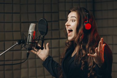 Mikrofonlu bir kadın müzik stüdyosunda dublaj yapmak için ses kaydediyor.