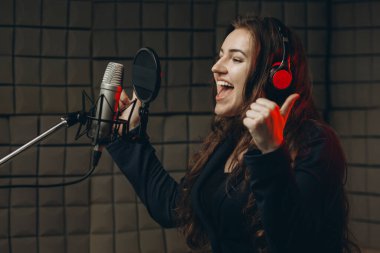 Mikrofonlu bir kadın müzik stüdyosunda dublaj yapmak için ses kaydediyor.