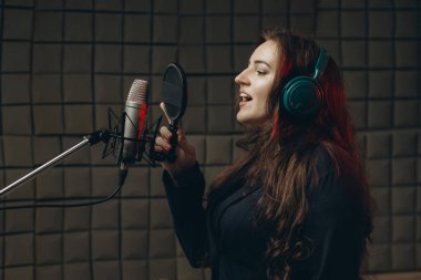 Mikrofonlu bir kadın müzik stüdyosunda dublaj yapmak için ses kaydediyor.