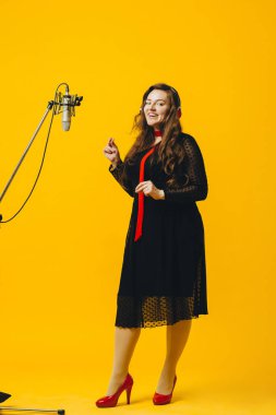 Eğlenen neşeli esmer kadın şarkıcı şarkı söylüyor. Sarı arka planda mikrofonla neşeli şarkılar söylerken kulaklıklı beyaz kadın pop sanatçısı.