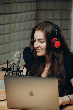 Ses stüdyosundaki genç kadın sesini profesyonel mikrofona kaydediyor. Çevrimiçi radyo ve podcast kavramı.