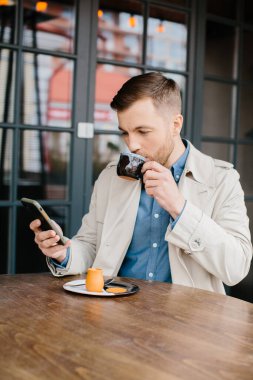 Kafede oturan genç adamın cep telefonundan mesaj okurken çekilmiş bir fotoğrafı..
