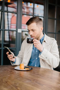 Kafede oturan genç adamın cep telefonundan mesaj okurken çekilmiş bir fotoğrafı..