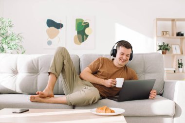 Yakışıklı adam kanepede uzanıyor ve kucağında çalışıyor.