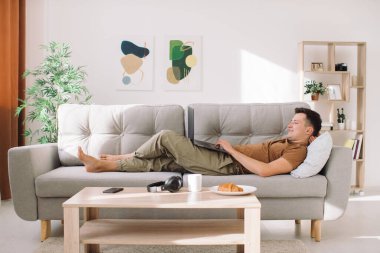 Yakışıklı adam kanepede uzanıyor ve kucağında çalışıyor.