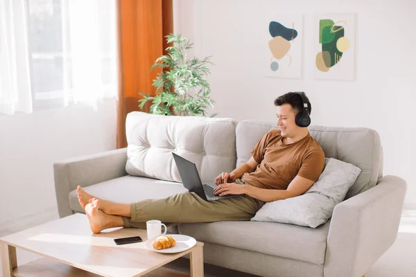 Relaxed Young Guy Wireless Headphones Lying Sofa Minimalistic Living Room — Stock Photo, Image