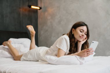Relaxed young woman using cell phone in bed - stock photo