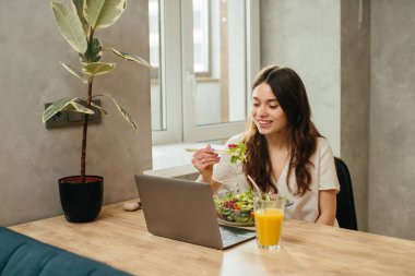 Young woman eating salad while sitting in kitchen - stock photo