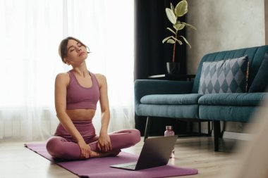 Yoga yapan çekici genç bir kadın evde yoga germe hareketleri yapıyor. Kişisel izolasyon internetteki yararlı, eğlenceli ve eğitimli bir şey. Sağlıklı yaşam tarzı kavramı.